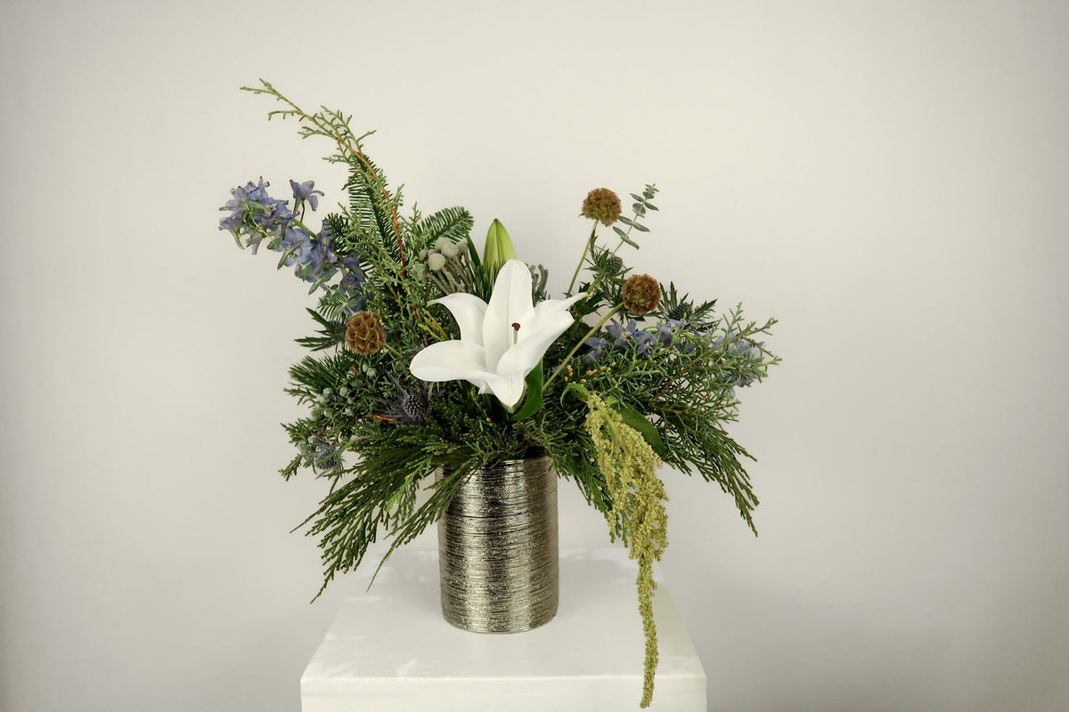 Floral arrangement with a white flower in a metallic vase on a white pedestal against a light gray background