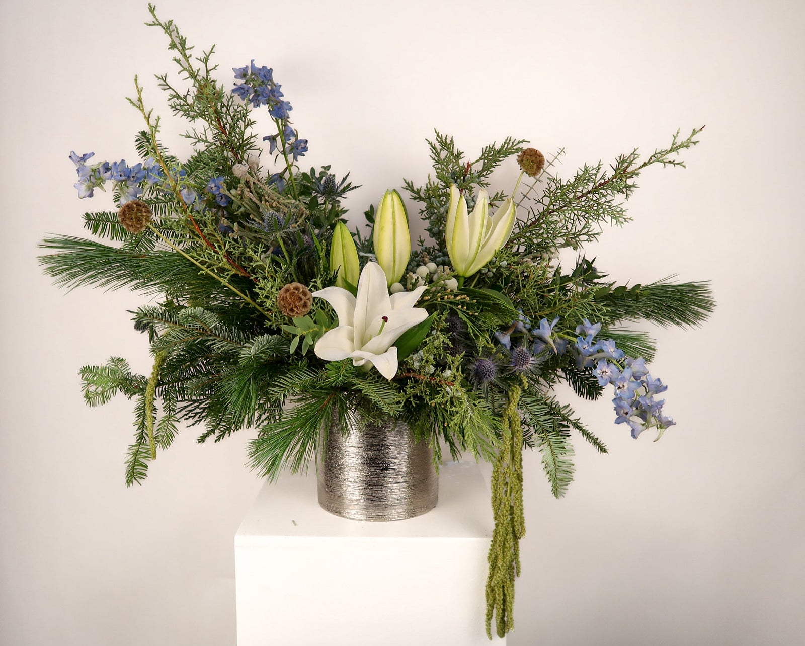 Floral arrangement with greenery and white lilies in a metallic container on a white background