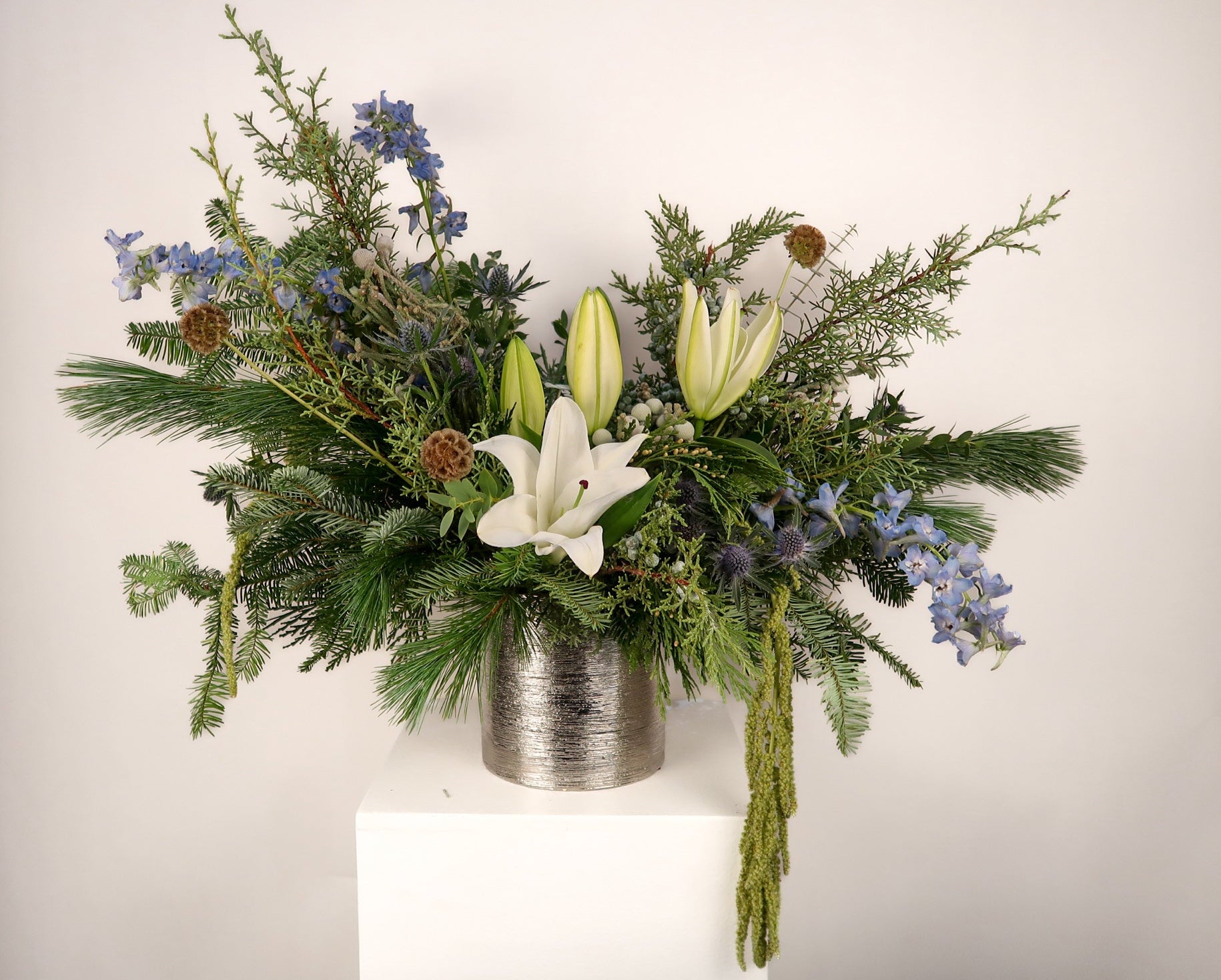 Floral arrangement with greenery and white lilies in a metallic container on a white background