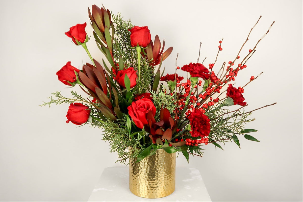 Bouquet of red flowers with greenery in a gold vase on a white background